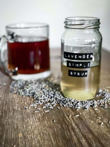 lavender simple syrup in a jar in front of a coffee cup. lavender buds on the table