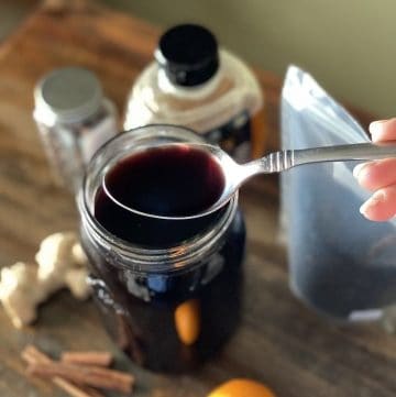 Syrup on a spoon over ingredients for elderberry syrup