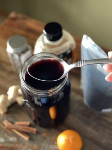 Syrup on a spoon over ingredients for elderberry syrup