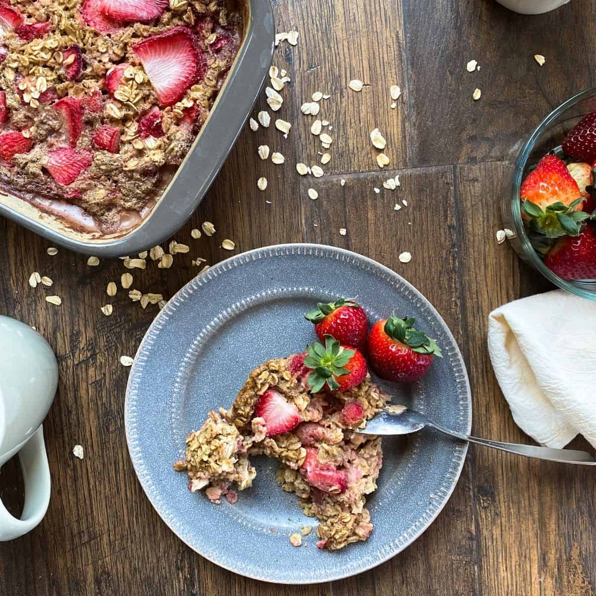 top down view of strawberry baked oatmeal. pan in one corner, and plate with oatmeal in center.