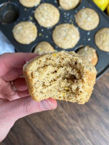 Lemon poppy seed muffin with a bite taken out of it. Pan of muffins in the background