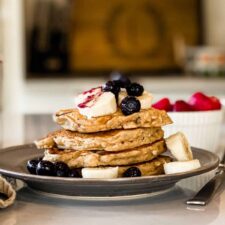 Stack of vegan oatmeal banana pancakes topped with blueberries, banana, syrup.
