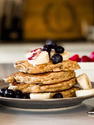 Stack of vegan oatmeal banana pancakes topped with blueberries, banana, syrup.