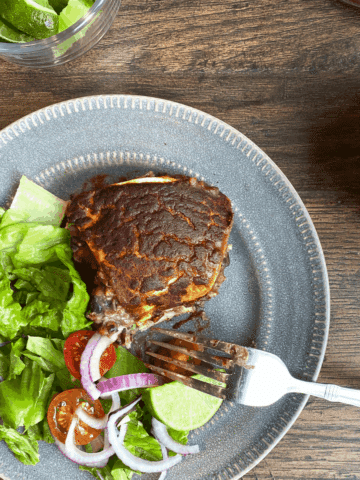 Vegan enchilada casserole on a plate with toppings: lettuce, onion, tomato, and lime.