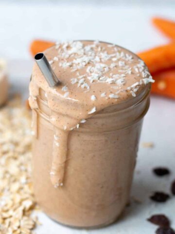 carrot banana smoothie in a mason jar with ingredients in the background. Topped with shredded coconut. metal straw in smoothie.