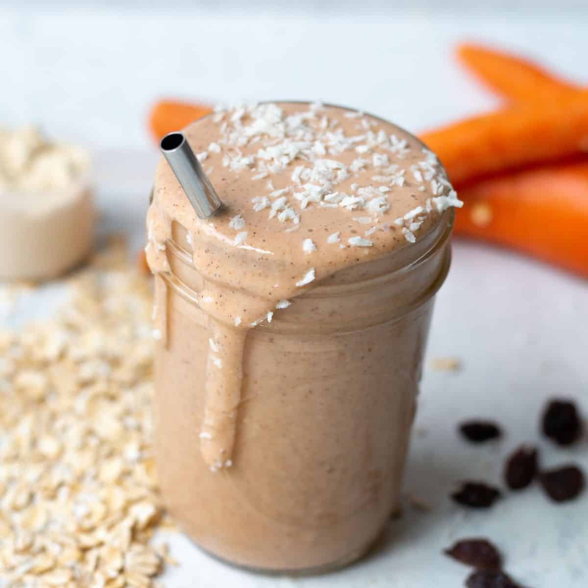 carrot banana smoothie in a mason jar with ingredients in the background. Topped with shredded coconut. metal straw in smoothie.