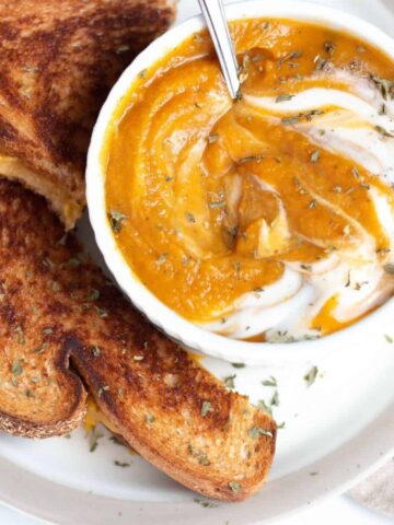 Pumpkin and sweet potato soup with sour cream swirled into it served with a vegan grilled cheese sandwich