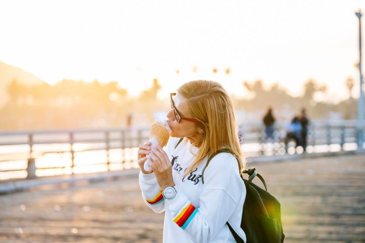 Woman enjoying an ice cream, guilt free on her intuitive eating journey. Wearing sunglasses and looking out over a boardwalk. 