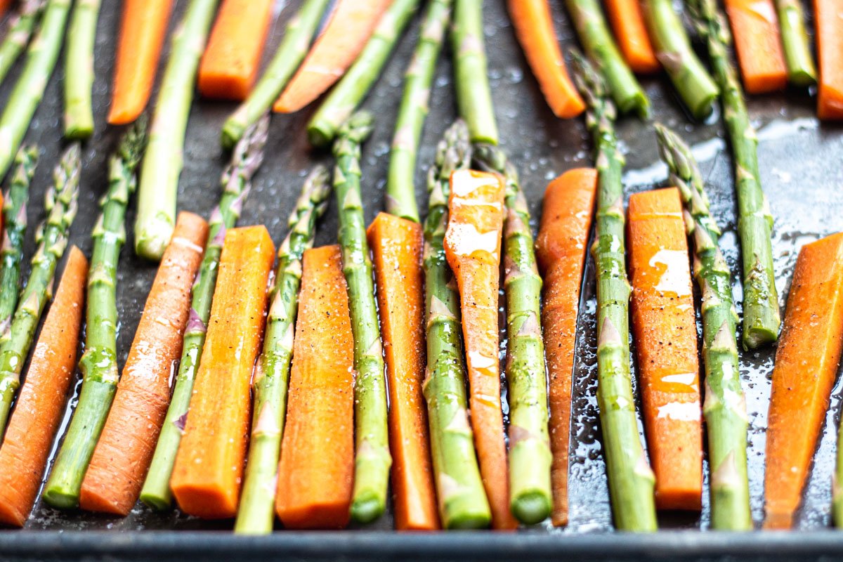 a sheet pan with raw carrots and asparagus lined up, drizzled with olive oil and sprinkled with salt and pepper. 