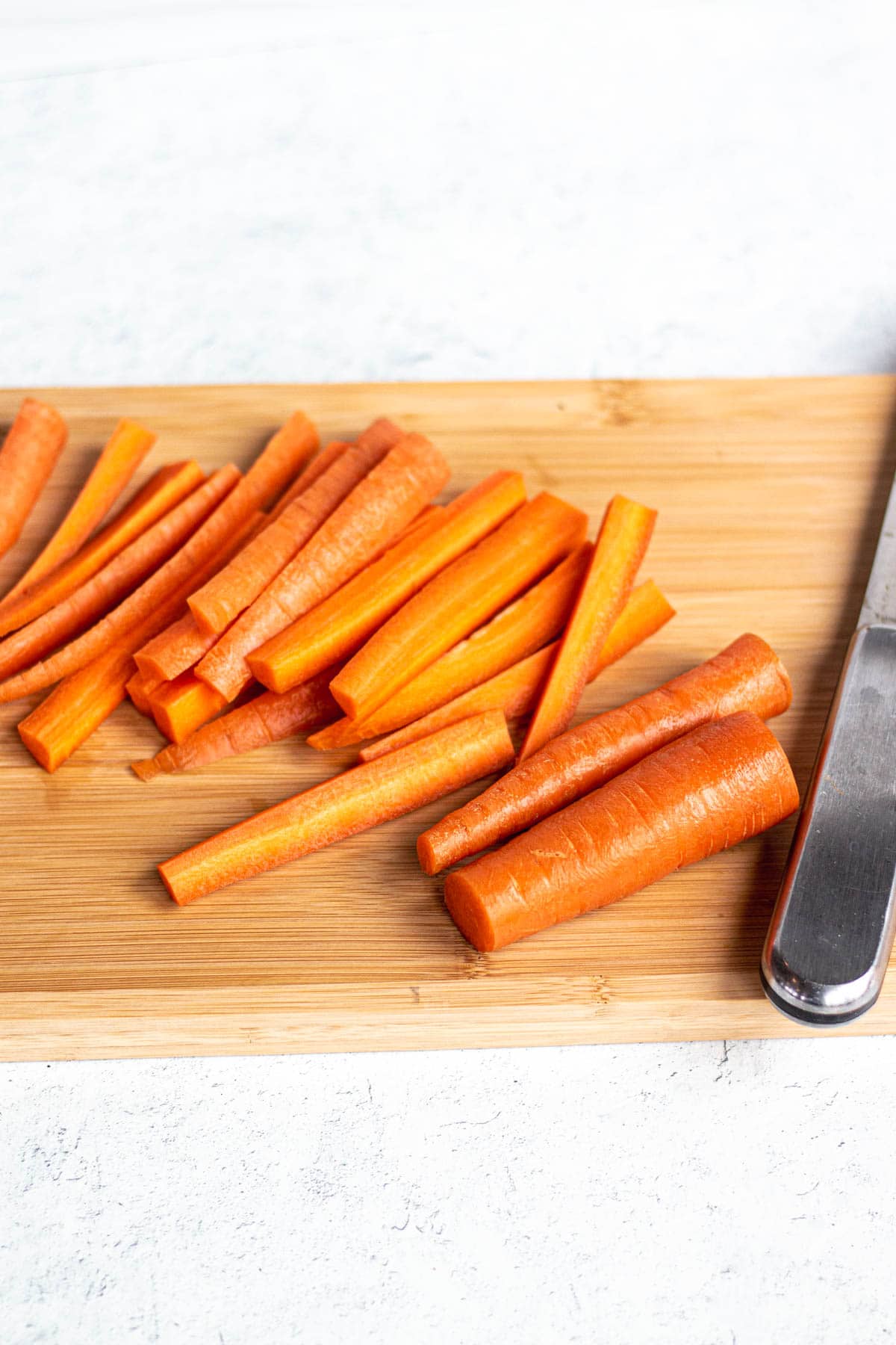Carrots on a wooden cutting board, some whole and some sliced into ½ inch thickness. 