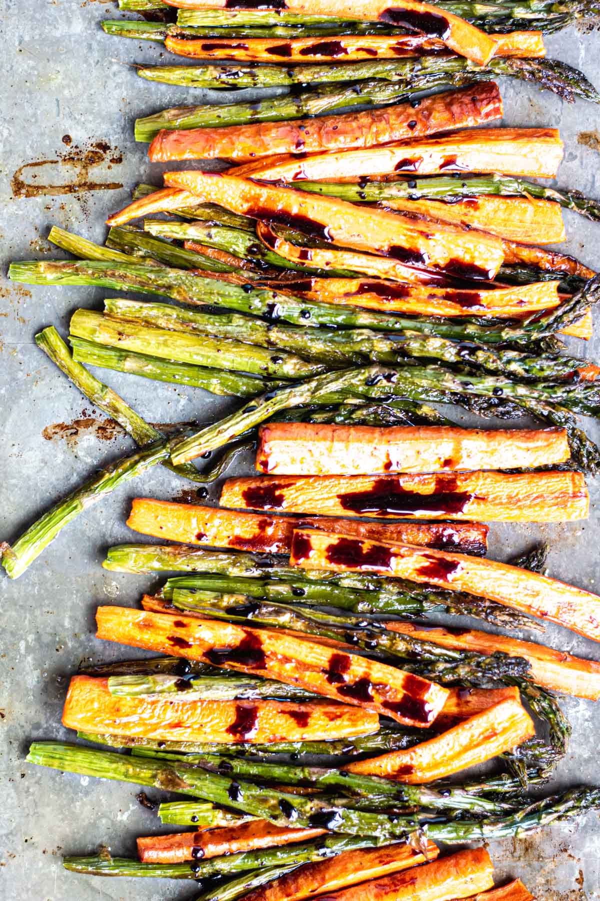 a sheet pan with roasted carrots and apsaragus lined up and drizzled with a thick balsamic glaze. 