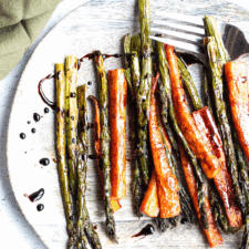 roasted carrots and asparagus covered in balsamic glaze drizzle on a wooden plate.