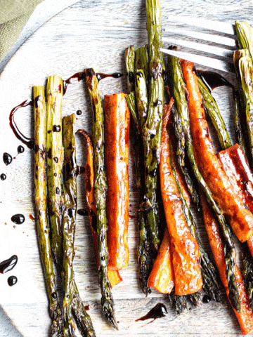 roasted carrots and asparagus covered in balsamic glaze drizzle on a wooden plate.