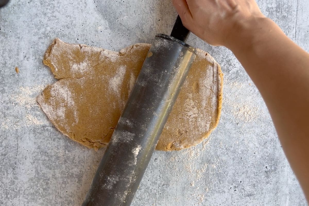 rolling out the fig roll cookie dough with a gray rolling pin on top of a concrete table. 