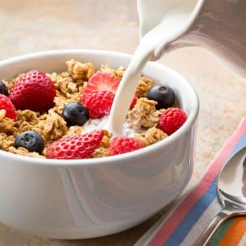 milk being poured into a bowl of high fiber cereal topped with berries