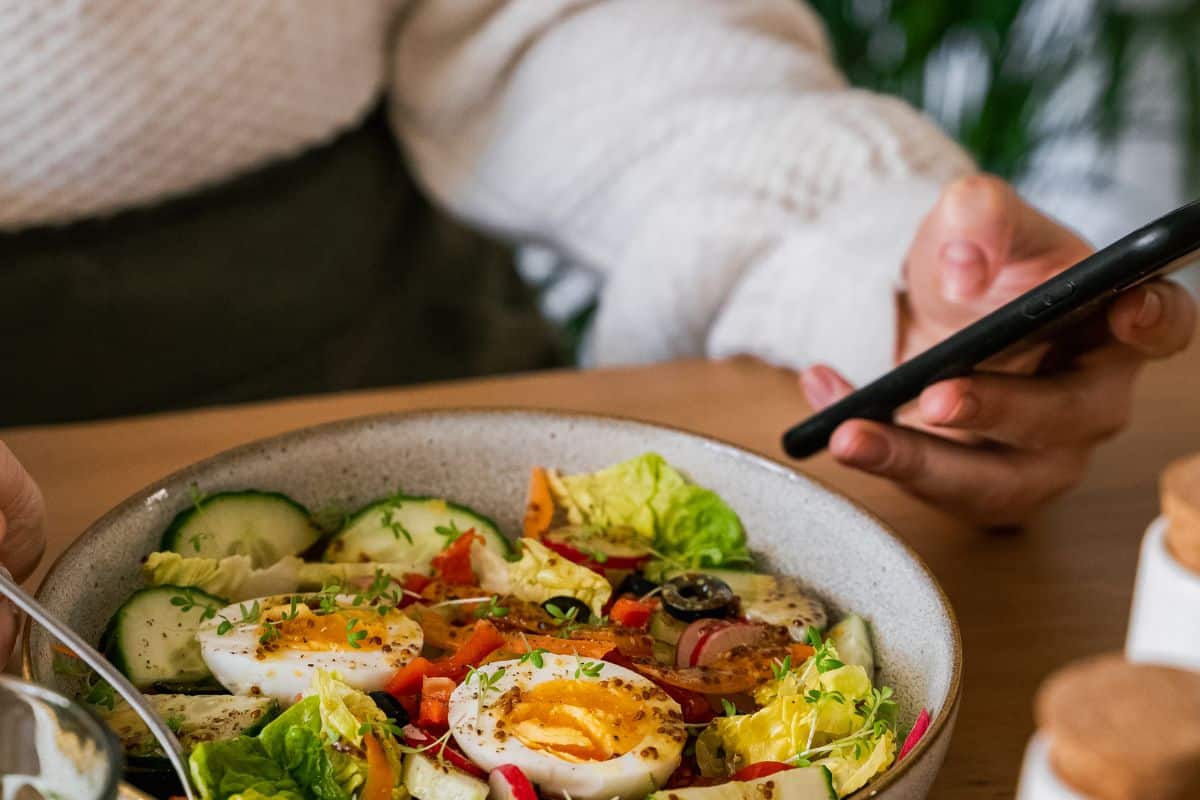 a woman eating a bowl of salad while looking at her phone. 