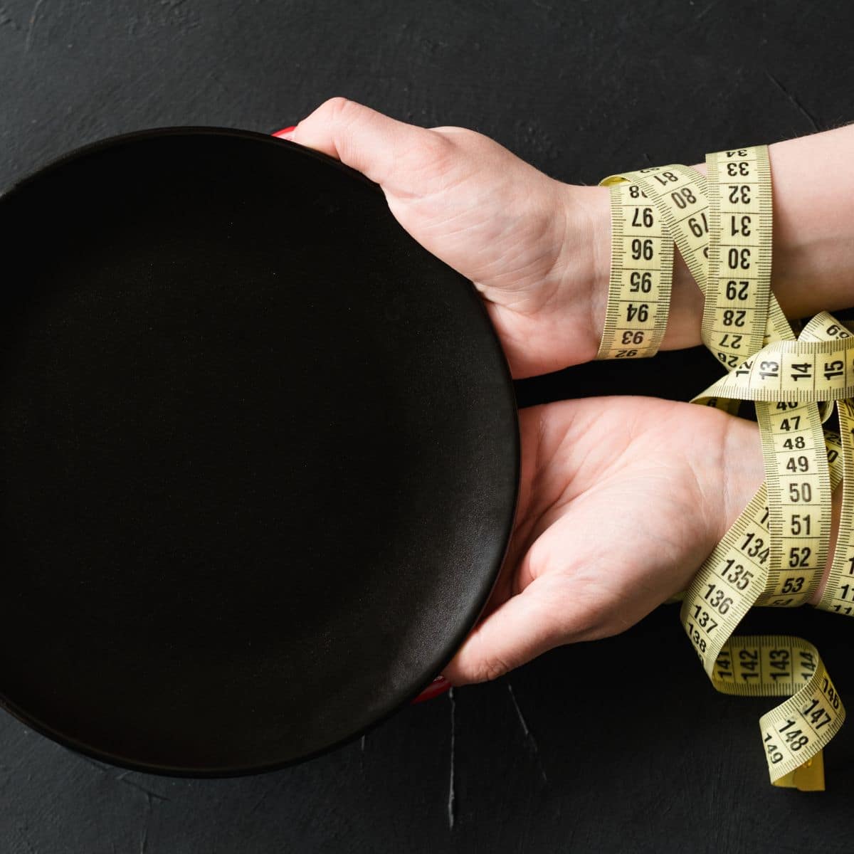 a woman's hands holding an empty plate with a measuring tape wrapped around her wrists. 