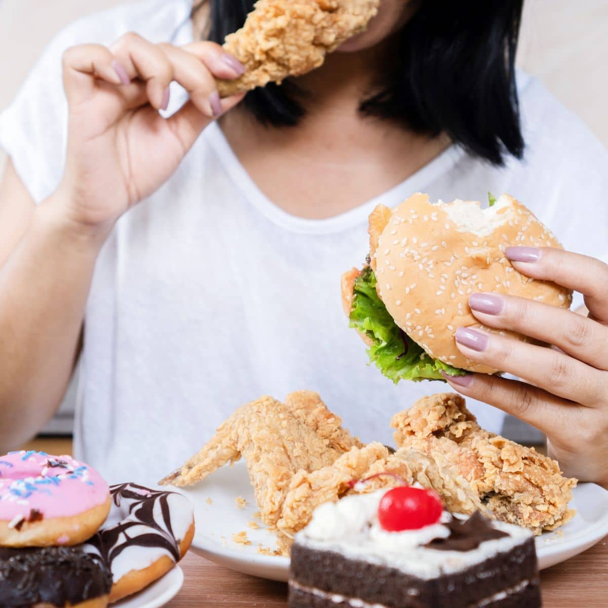 woman binge eating on plates of fried foods and desserts