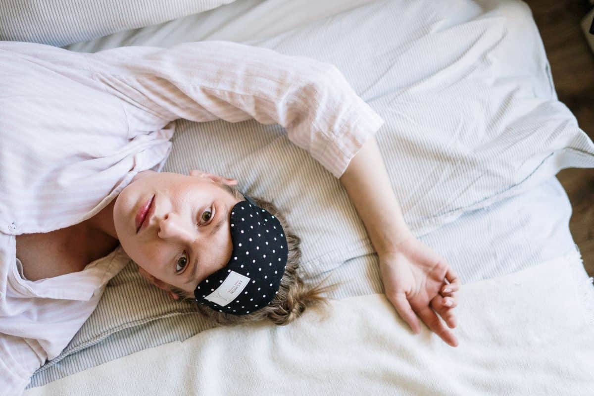 a woman laying on a bed with sleep mask, unable to sleep.