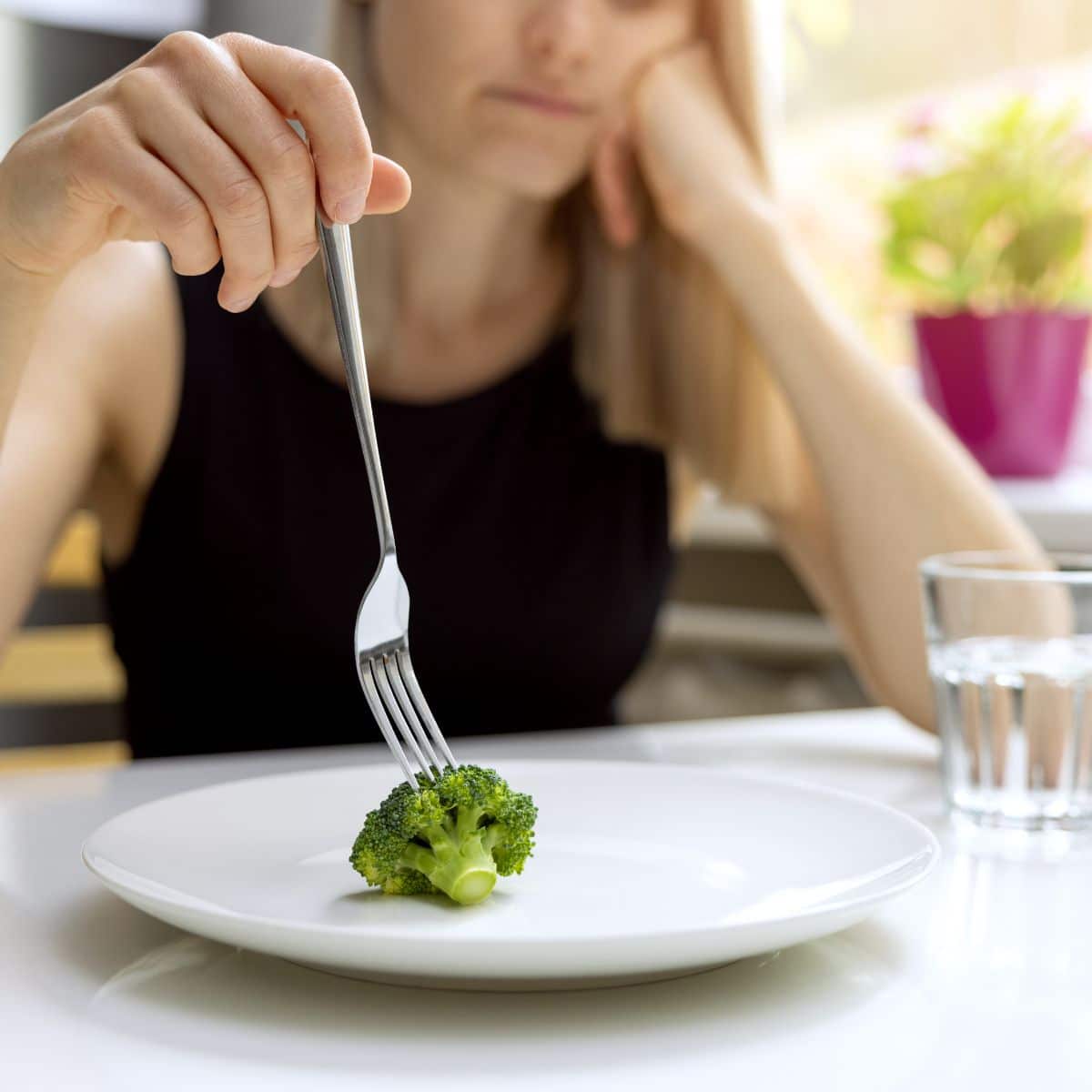 woman in a binge restrict cycle, putting a single piece of broccoli on a fork. 