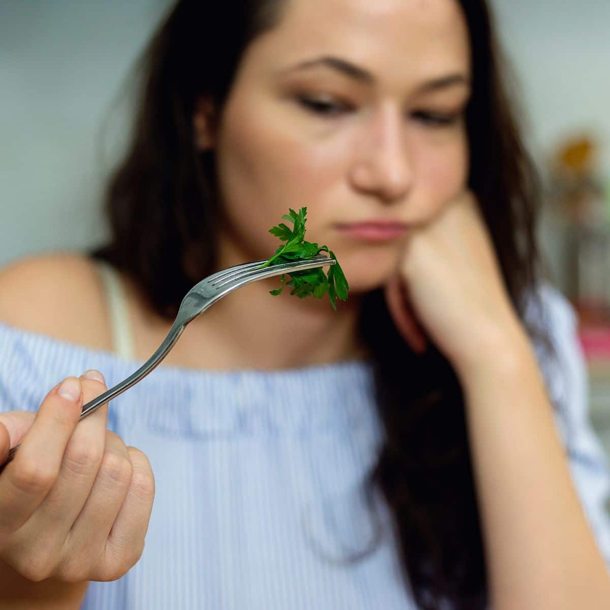 woman upset looking at a leafy green on her fork while dieting.