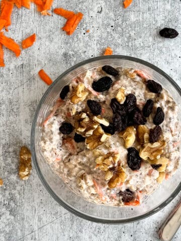 A bowl of carrot cake overnight oats topped with raisins, walnuts, and carrots.