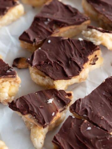 Frozen chocolate peanut butter banana bark with layers of mashed banana, peanut butter, and melted chocolate, topped with optional toppings like sea salt and crushed peanuts, served on parchment paper.