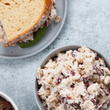 A bowl of chicken salad without mayo next to a sandwich packed with the same filling.