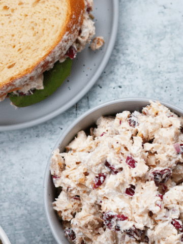 A bowl of chicken salad without mayo next to a sandwich packed with the same filling.