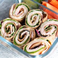 Turkey and cheese roll ups neatly arranged inside a clear food container, showcasing a fresh, tasty sandwich.