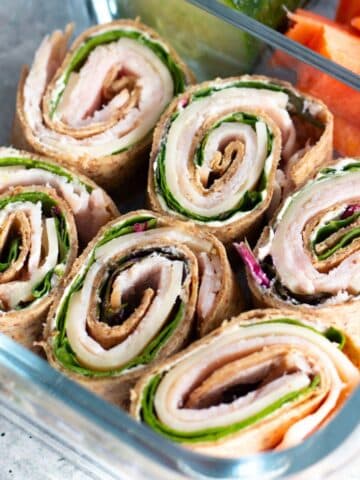 Turkey and cheese roll ups neatly arranged inside a clear food container, showcasing a fresh, tasty sandwich.