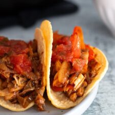 Two skillet chicken fajitas made with shredded rotisserie chicken, sautéed bell peppers, and onions, wrapped in warm tortillas on a white plate.