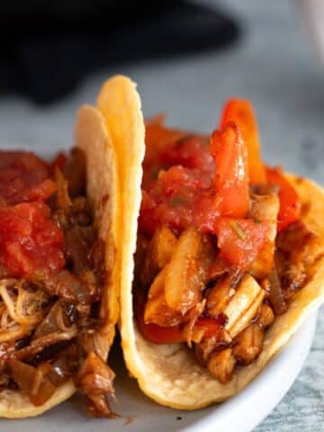 Two skillet chicken fajitas made with shredded rotisserie chicken, sautéed bell peppers, and onions, wrapped in warm tortillas on a white plate.