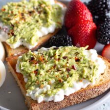 Avocado cottage cheese toast on a white plate, topped with everything bagel seasoning for a quick and easy breakfast.