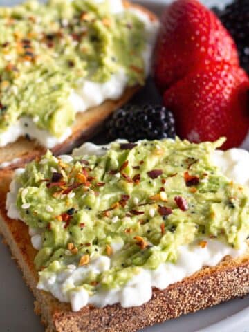 Avocado cottage cheese toast on a white plate, topped with everything bagel seasoning for a quick and easy breakfast.