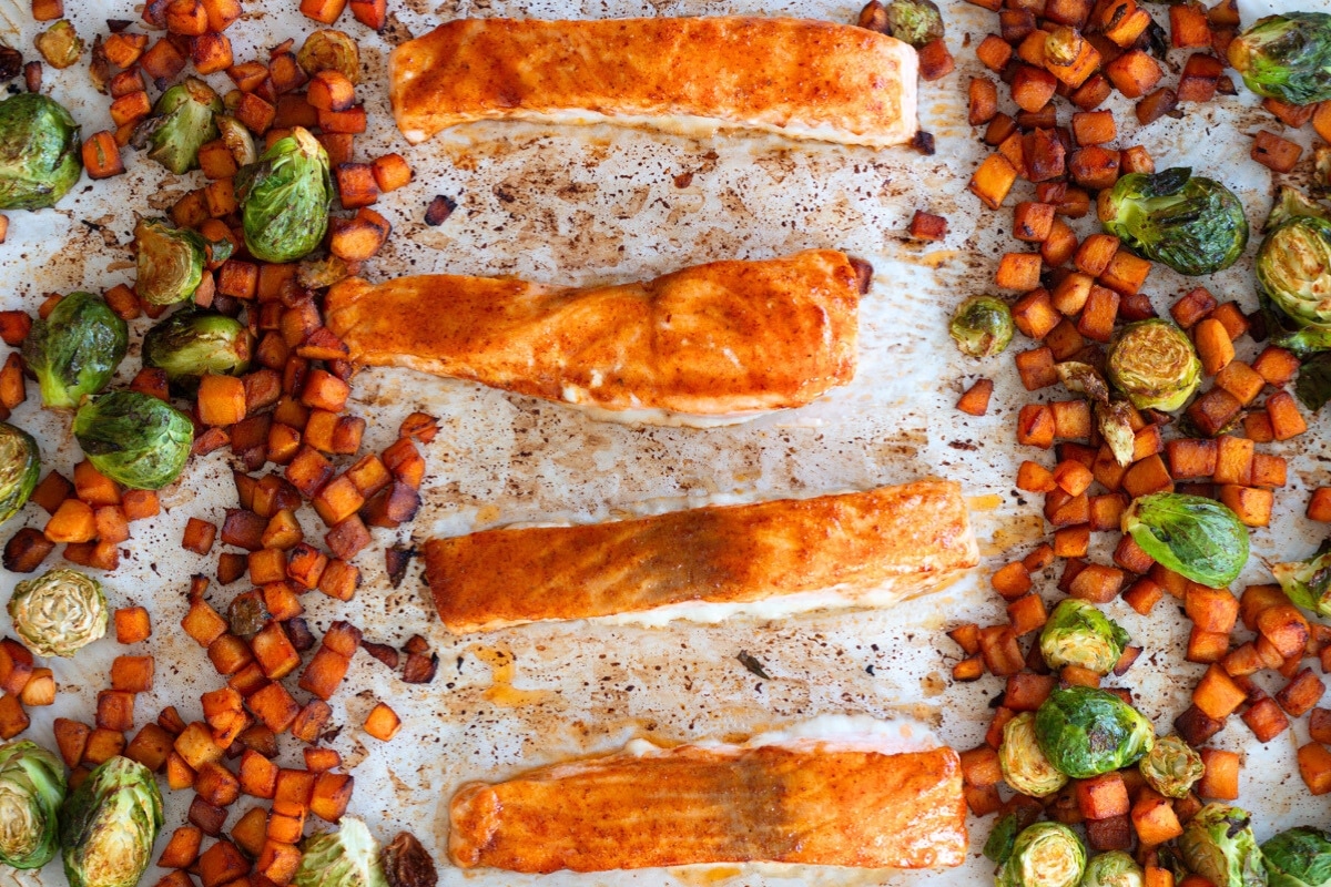 Sheet pan salmon with veggies fresh out of the oven, featuring roasted butternut squash and Brussels sprouts, all coated in a smoky-sweet glaze for a nutritious and practical one-pan meal.