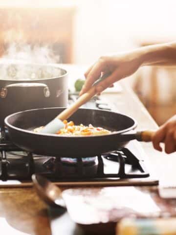 a busy mom cooking dinner over the stove with multiple pots and pans going.